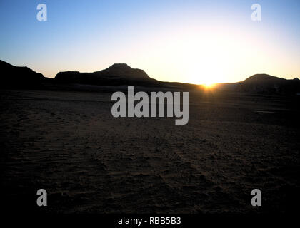 Sun setting behind desert rock formations Stock Photo