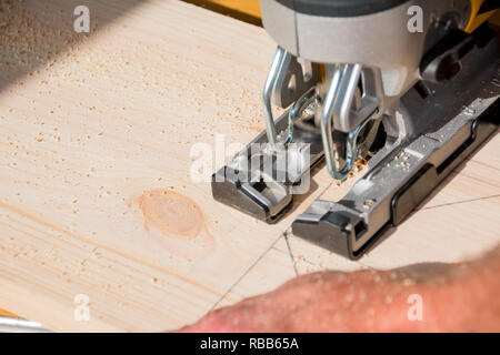 young man carpenter builder working with electric jigsaw and wood.hobby concept.DIY acronym cut out in OSB panel with electric jigsaw.Woodworker cutting a piece of wood Stock Photo