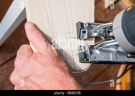 young man carpenter builder working with electric jigsaw and wood.hobby concept.DIY acronym cut out in OSB panel with electric jigsaw.Woodworker cutting a piece of wood Stock Photo