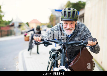 Active senior couple with electrobikes standing outdoors on a road in town. Stock Photo