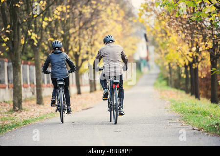 A rear view of senior couple with electrobikes cycling outdoors on a road. Stock Photo