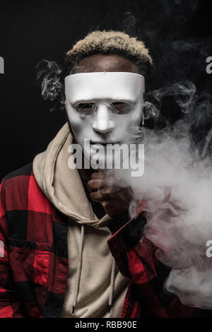 Young african man with mask on face vape electronic cigarette cloud by using a mod, smoke tricks of vaping device background. Stock Photo