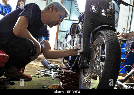 Side view portrait of man working in garage repairing motorcycle Stock Photo