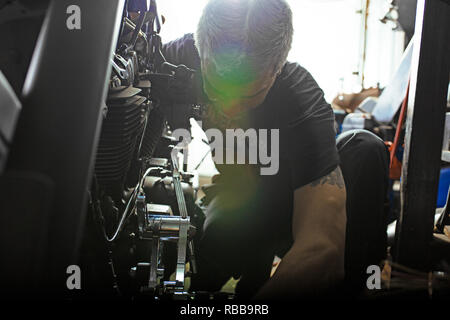 Side view portrait of man working in garage repairing motorcycle Stock Photo