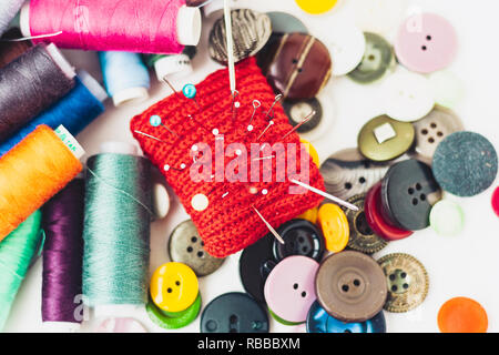 Red knitted needle pad for sewing, sewing buttons and colored thread coils on white background Stock Photo