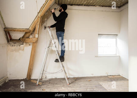 Handyman standing on a ladder and renovating a home, using tools like a hammer Stock Photo