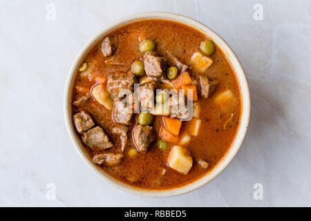 Caption/Description: Tasty Hungarian Hot Goulash Soup Bograch or Gulas Lamb Meat Stew with Whole Grain Bread on Wooden Surface at Restaurant. Traditio Stock Photo