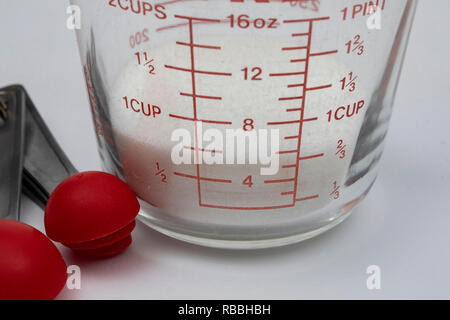 White cane sugar in a measuring cup with measuring spoons. Stock Photo