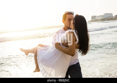 Young man carrying his girlfriend in his arms at the beach