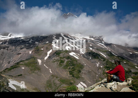 WA15686-00...WASHINGTON - Hiker watching the clouds move across the face of Mount Rainier from the summit of Pyramid Peak in Mount Rainier National Pa Stock Photo