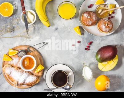 Breakfast served with coffee, orange juice, croissants, donuts and fruits on concrete background. Top view Stock Photo