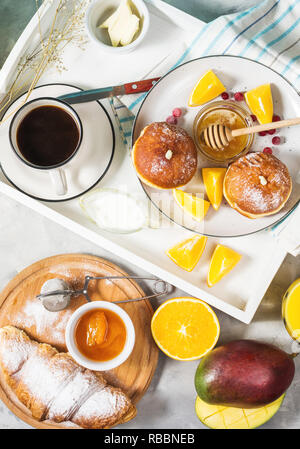 Breakfast served with coffee, orange juice, croissants, donuts and fruits on white tray. Top view Stock Photo