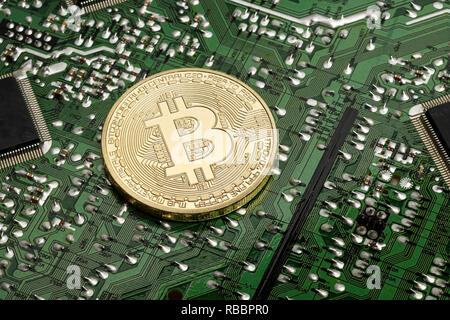 A Bitcoin coin resting on a printed circuit board Stock Photo