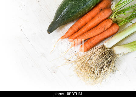 carrots, leek and zuccini freshly harvested from the vegetable garden on white painted wood with copy space, corner background from above fades to whi Stock Photo