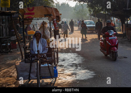 A rickshaw-wala (rickshaw-man) waits for passengers in this morning scene in JJ Colony Madanpur Khadar, New Delhi while commuters rush past. Stock Photo