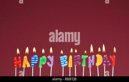 Happy Birthday candles against a dark red background Stock Photo