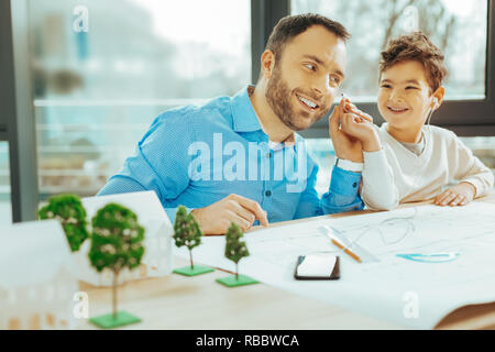 Nice music. Positive happy kid sitting next to his cheerful father and smiling while sharing earphones with him Stock Photo
