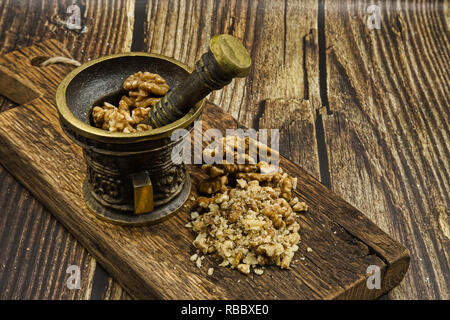 Old-fashioned mortar with pestle and walnuts whole and shredded on old wooden background in vintage style.Close, horizontal view. Stock Photo