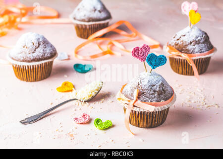 Tasty delicious homemade muffin on light pink living coral stone concrete surface with knitting hearts, copy space. Sweet food for valentines day. Stock Photo