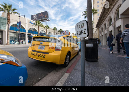 People walking down Hollywood Boulevard past a yellow Toyota Prius taxi cab in a taxi zone in Los Angeles, California, USA Stock Photo