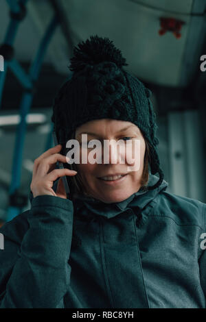 Beautiful adult woman talking on mobile phone in public bus in cold winter afternoon