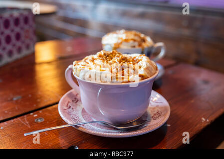 Two cups of fresh hot chocolate topped with whipped cream and salted caramel on a brown wooden table. Stock Photo