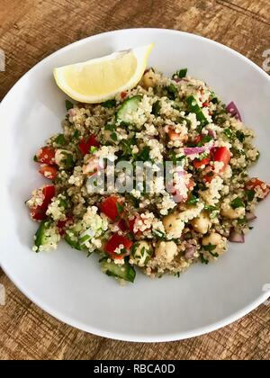 A healthy and colourful vegan quinoa salad with lemon wedge on a wooden table Stock Photo