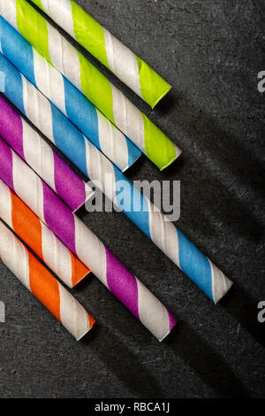 Multicoloured drink straws on dark stone background. Vibrant colours contrast on natural light. Paper made straws. Close-up macro shot. Stock Photo