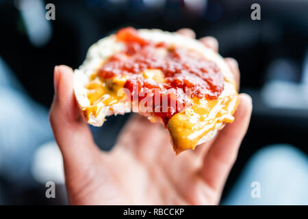 Macro closeup of hand holding one rice cake in car road trip blurry background topped with peanut butter, strawberry jam, vegan dessert snack Stock Photo