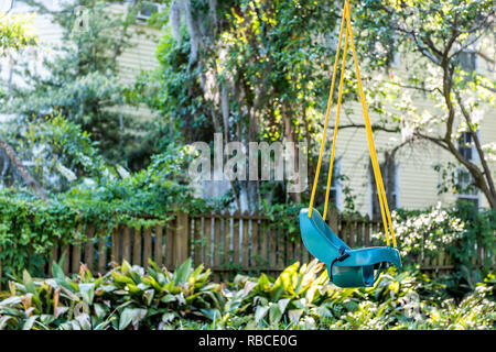 Patio green southern garden with hanging yellow and blue plastic toddler child swing in outdoor backyard porch of home and nobody in Charleston house Stock Photo