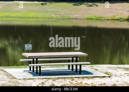 Rest area stop with lake pond by highway road in North Carolina with empty picnic table in park and no fishing sign during day Stock Photo