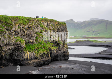 Myrdal, Iceland - June 14, 2018: Reynisfjara black sand beach and volcanic rocky cliff formation with seashore coastline and people, tourists standing Stock Photo