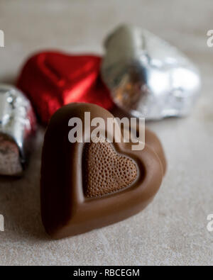 Close up view of chocolate hearts unwrapped on stone tile.  Red and silver hearts in background.  Close up view. Room for Copy Stock Photo