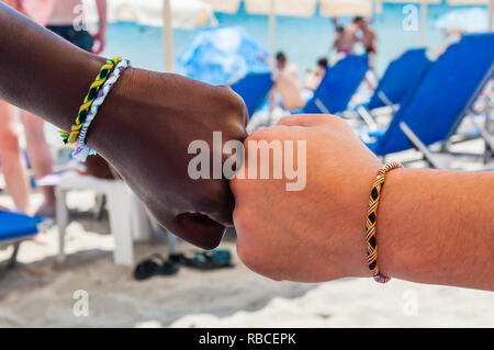 Two fists of two different ethnicity people with braided bracelets from colored threads on each of the wrists touching each other in a friendship and  Stock Photo