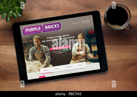 The website of Purple Bricks is seen on an iPad tablet, on a wooden table along with an espresso coffee and a house plant (Editorial use only). Stock Photo