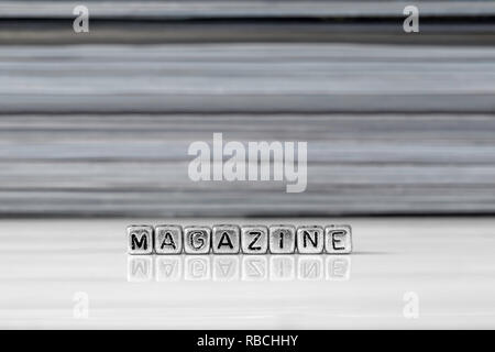Magazine on beads with magazines stacked in the background reflected on a white surface Stock Photo