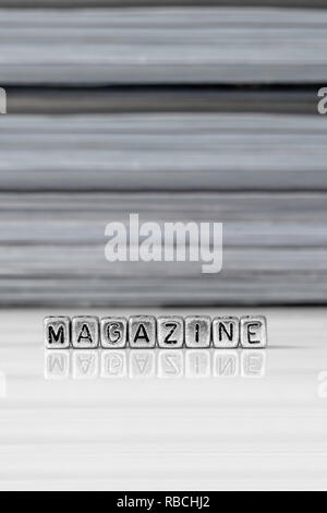 Magazine on beads with magazines stacked in the background reflected on a white surface Stock Photo
