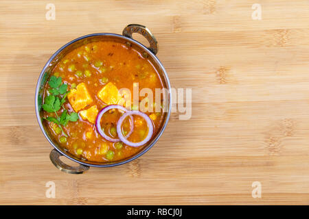 Indian Food or Indian Curry or Kadai Paneer in a copper brass serving bowl lying on wooden surface Stock Photo