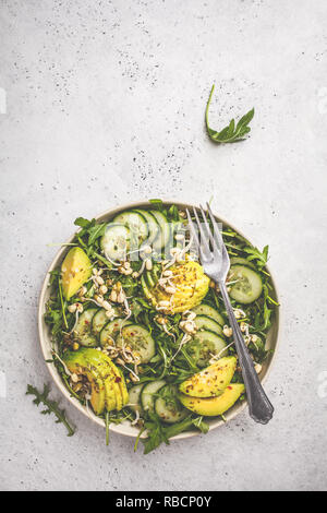 Healthy green salad with avocado, cucumber and arugula in white dish. Plant based diet concept.