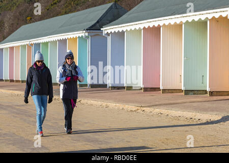 Bournemouth, Dorset, UK. 9th January 2019. Uk weather: sunny with blue skies, although coldish, day at Bournemouth, as visitors head to the beach for some fresh air and exercise. Two women walking along promenade past colourful beach huts. Credit: Carolyn Jenkins/Alamy Live News
