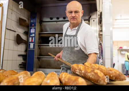 Dachsbach, Germany. 09th Jan, 2019. Arnd Erbel, master baker and confectioner and owner of the family bakery of the same name, lays baguettes from the oven on a baking board in the bakery of the company. Founded in the 17th century, the bakery has made a name for itself in the USA with bread, pretzels and gingerbread. Credit: Daniel Karmann/dpa/Ģ����ý Live News Stock Photo