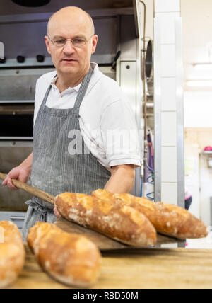 Dachsbach, Germany. 09th Jan, 2019. Arnd Erbel, master baker and confectioner and owner of the family bakery of the same name, lays baguettes from the oven on a baking board in the bakery of the company. Founded in the 17th century, the bakery has made a name for itself in the USA with bread, pretzels and gingerbread. Credit: Daniel Karmann/dpa/Ģ����ý Live News Stock Photo