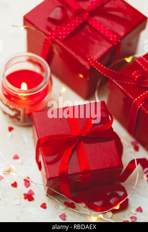 Gift red boxes with red bow ribbons, candles, lights garland and hearts on light background for Valentines day. Stock Photo