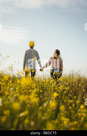Rear view of couple standing together holding hand and looking at a view. Loving couple in meadow admiring the view. Stock Photo