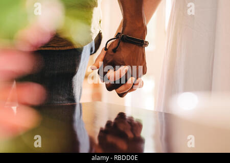 Close up of young man and woman holding hands. Cropped of interracial couple on date holding hands, focus on hand in hand. Stock Photo
