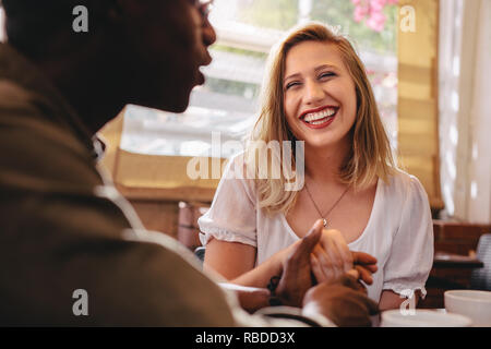 Happy young woman holding hand of her boyfriend at coffee shop. Loving couple on a date at cafe. Stock Photo