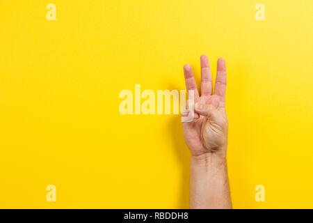Man hand showing three fingers on yellow background. Number two symbol Stock Photo