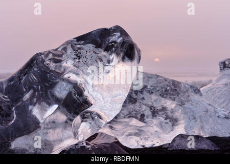 Striking ice formations are staged by evening clouds lit by a cloud cover in red and yellow shades, the setting sun is visible - Location: Iceland, so Stock Photo