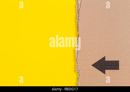 Brown corrugated cardboard ragged edge with black arrow on yellow background Stock Photo