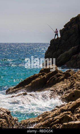 A brave fisherman sea fishing with a fishing rod standing on dangerous high cliffs with the ocean beneath Stock Photo